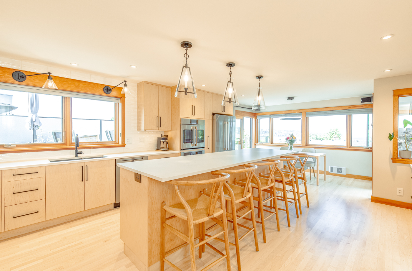 Four pendant lights positioned over a long kitchen island with seating in a bright modern kitchen.