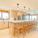 Contemporary open-concept kitchen remodel with waterfall quartz island, natural maple cabinetry, slab doors, and full-height upper cabinets with flat riser for a seamless built-in look