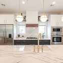 Two-tone townhouse kitchen renovation featuring Cambria Portrush quartz island, brass faucet, globe pendant lights, white shaker cabinets, dark lower cabinetry, and built-in stainless appliances.