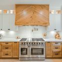 Two-tone kitchen range wall with Lectus Beckham maple shaker base cabinets stained Ginger, Nougat painted upper cabinets, white quartz countertops, subway tile backsplash, and custom wood range canopy